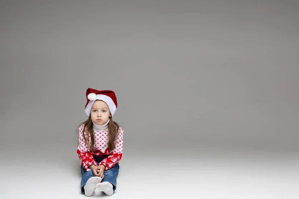 Gadis tak bahagia dengan topi dan sweater Santa yang meriah. — Stok Foto