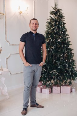 Neşeli beyefendi gülümsüyor ve Noel ağacının yanında duruyor.