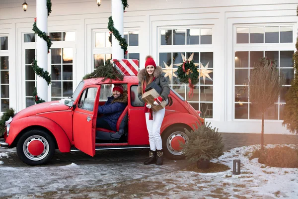 Young couple buys Christmas presents for their family and take them to home in a red car — 스톡 사진