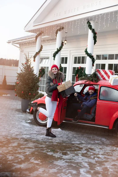 Young couple buys Christmas presents for their family and take them to home in a red car — 스톡 사진