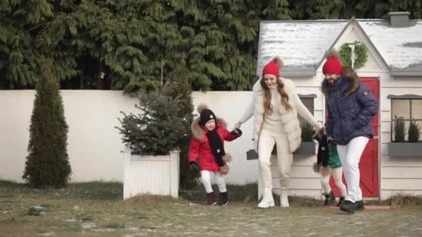 Xmas aile tatili, çocuklu genç ebeveynler Noel ağacı ve evin yakınında neşeli bir şekilde el ele koşuyorlar. — Stok video