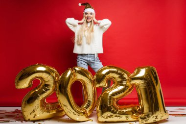 2021 numaralı büyük altın balonların yanında rahat elbiseli çekici bir kadın seviniyor.