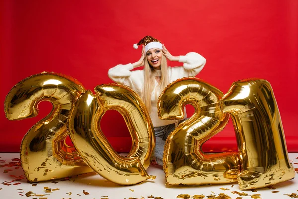 Büyük altın balonların yanında rahat elbiseli çekici bir kadın. 2021 numara bayram ediyor ve dizlerinin üzerinde duruyor. — Stok fotoğraf