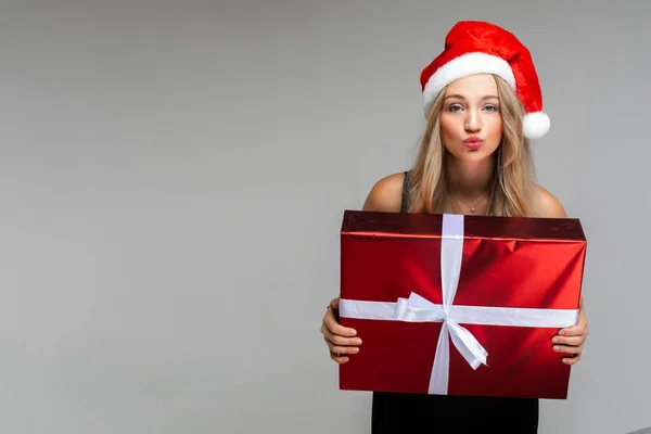 Radosna kobieta w czarnej sukience i świątecznym kapeluszu raduje się pudełkiem z prezentem świątecznym — Zdjęcie stockowe
