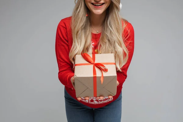 Beskuren närbild av leende blond långhårig flicka i röd tröja ger närvarande på grå bakgrund med kopia utrymme — Stockfoto