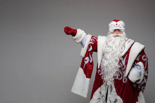 Weihnachtsmann zeigt mit der Hand auf leeren Raum auf grauem Studiohintergrund mit Kopierplatz für Weihnachtswerbung — Stockfoto