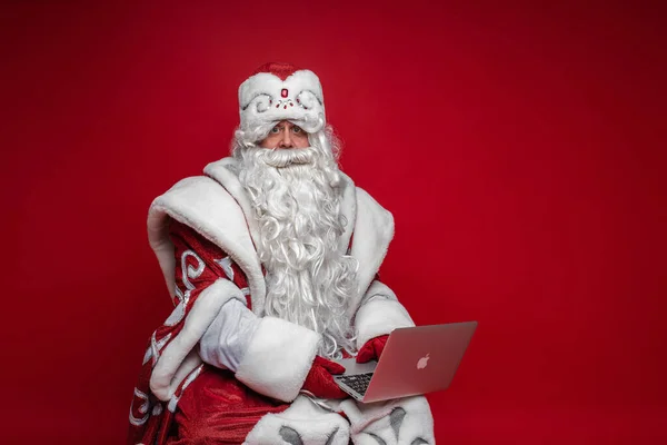Papai Noel usando laptop se preparando on-line para xmas e feriado de ano novo no fundo vermelho — Fotografia de Stock
