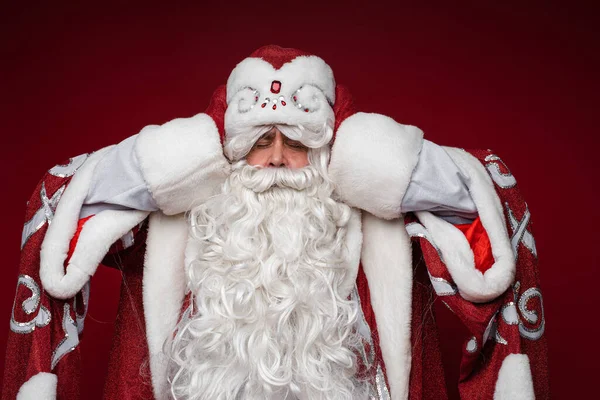 Санта-Клаус устает и хватает голову от головной боли, закрытые глаза, студийный портрет на красном фоне — стоковое фото