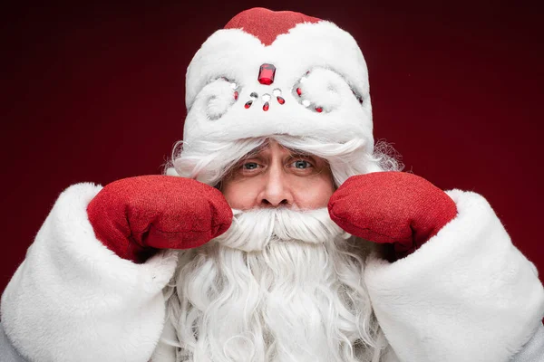 Papai Noel cabelos grisalhos macho sênior em mitenes mostrar seu bigode, close up retrato de estúdio no fundo vermelho — Fotografia de Stock