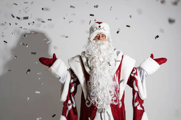 Santa claus under festive xmas confetti showing welcome gesture, studio holiday portrait for congratulations — Stock Photo, Image