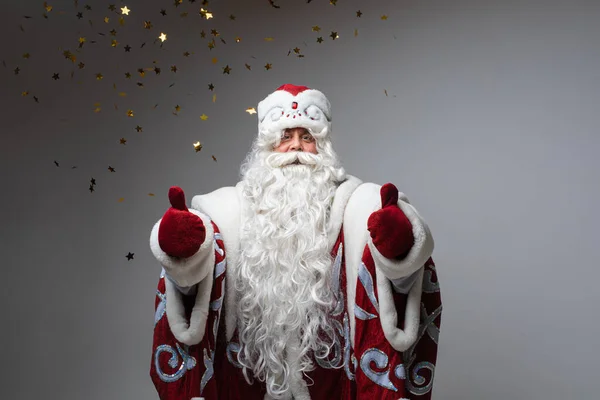 Санта-Клаус под золотыми конфетти позирует с большим пальцем на сером фоне студии, праздничные рождественские и новогодние эмоции — стоковое фото