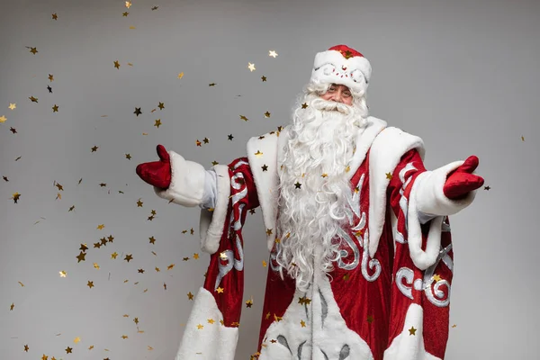Santa Claus bajo estrellas doradas confeti hace gesto de bienvenida sobre fondo gris, tarjeta para Navidad y diseño de año nuevo —  Fotos de Stock