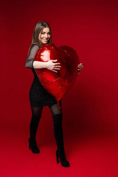 Glimlachende mooie vrouw knuffelen rode ballon in studio — Stockfoto