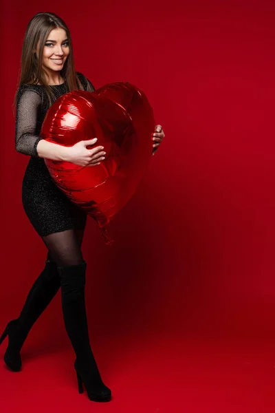 Knappe vrouw met recht donker haar houdt een grote rode lucht ballon en glimlacht — Stockfoto