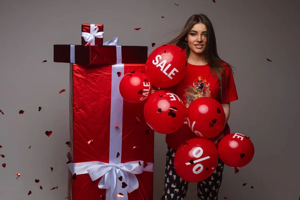 아름다운 코카서스 여성이 빨간 상자 옆에 서 있습니다. 빨간 발론을 잔뜩 선물하면서 팔리고 인과응보를 바르고 있죠. — 스톡 사진