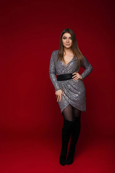 Slim gadis muda Kaukasia berambut panjang dengan gaun perak meriah berpose di latar belakang merah dengan salinan ruang untuk iklan — Stok Foto