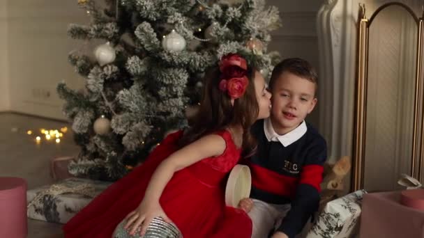 Mignons frères et sœurs petite fille et enfant garçon baisers assis près de l'arbre de Noël avec des cadeaux, Noël famille vacances concept — Video