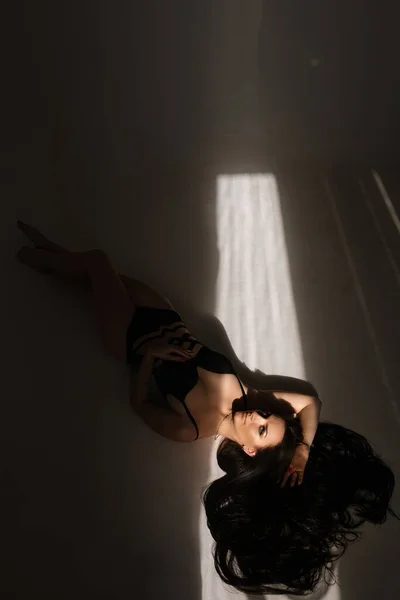 Affascinante bruna dai capelli lunghi giovane donna in lingerie nera biancheria intima elegante in posa sul pavimento alla luce del giorno, vista dall'alto — Foto Stock