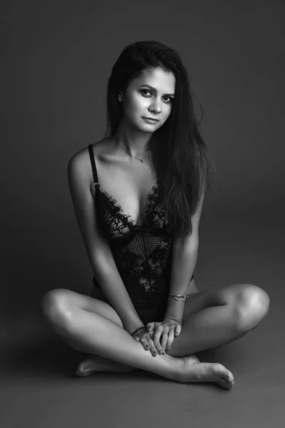Stijlvolle zwarte lingerie op pasvorm jong vrouwelijk model zitten op rode studio achtergrond, kopiëren ruimte voor ondergoed reclame — Stockfoto