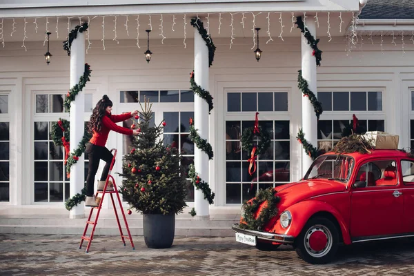사닥다리 위에 있는 한 여자 가집 앞에 있는 크리스마스 트리를 장식한다 — 스톡 사진
