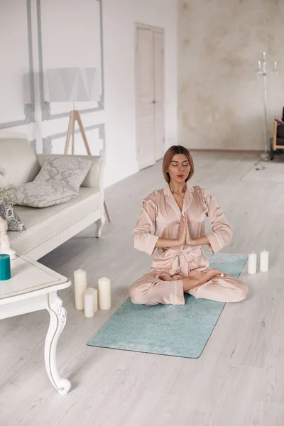 Dame im Pyjama praktiziert Yoga und sitzt zu Hause in besonderer Pose auf Teppich — Stockfoto