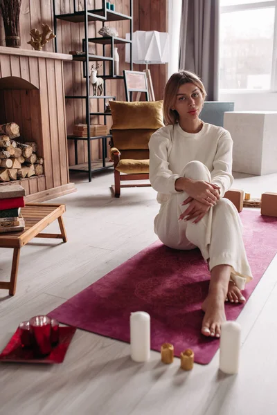 Молода леді позує, сидячи на килимку йоги — стокове фото