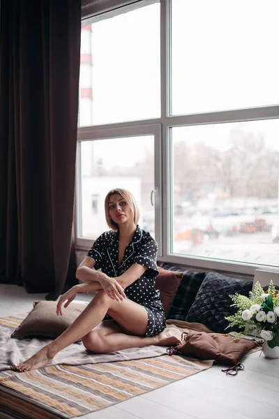 Красива жінка в піжамі сидить на дивані з подушками — стокове фото