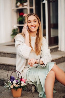 Mavi elbiseli neşeli genç bayan dışarıda çiçeklerle gülüyor.