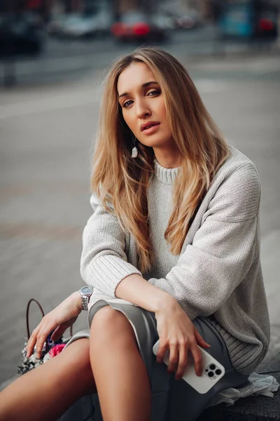 Mujer de negocios chica con estilo bastante joven con teléfono sentado, posando en la calle. Moda femenina, estilo casual y feminidad — Foto de Stock