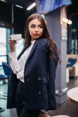 Beyaz bir fincan kahve ya da çayla çekici bir kadın yana bakıyor.