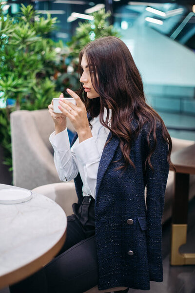 Pretty young woman drinks hot coffee in the cafe before hard working day