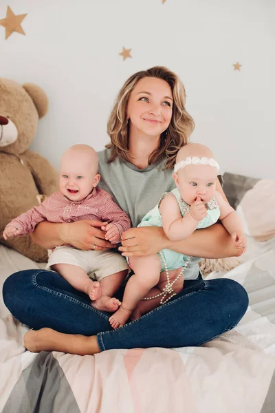 Mooie jonge moeder zit op de vloer met haar kinderen en glimlacht — Stockfoto