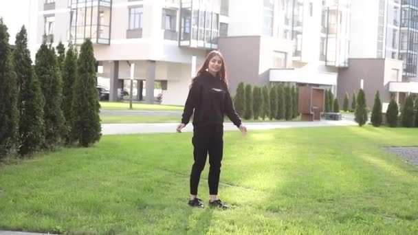 Glada flicka i svart kostym hoppar på gräsmattan. — Stockvideo