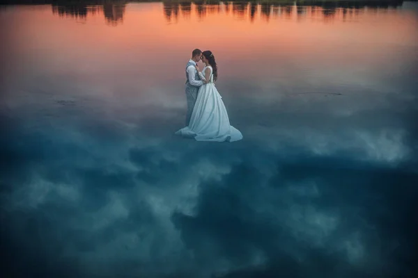 Pareja recién casada parada sobre el agua al atardecer. — Foto de Stock
