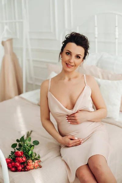 Mulher grávida atraente em vestido de seda toca sua barriga com sorriso feliz — Fotografia de Stock