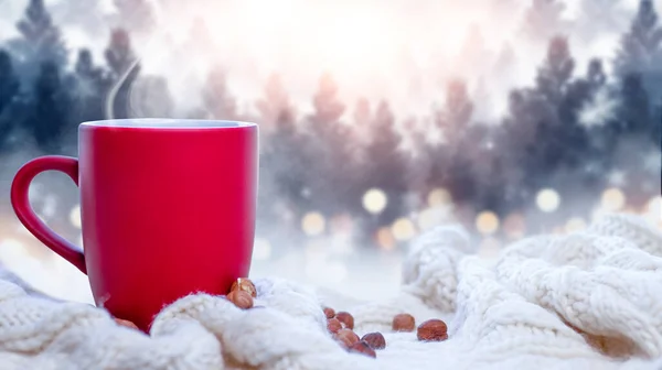 Red cup with coffee, tea on a snowy background, winter forest. A red cup against the background of a winter forest landscape on a soft, cozy scarf. Coffee, tea in the mountains.