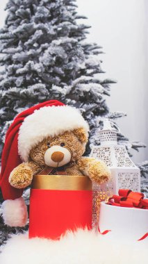 Yeni yıl iç kısımları, kar ağacı, gece feneri ve mumlar, hediyeler. Noel ve yeni yılın büyülü atmosferi. Oyuncak ayı Noel Baba şapkasıyla Noel ağacının yanındaki sandalyede oturuyor..