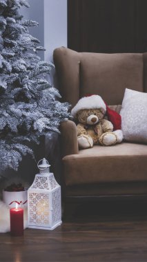 Yeni yıl iç kısımları, kar ağacı, gece feneri ve mumlar, hediyeler. Noel ve yeni yılın büyülü atmosferi. Oyuncak ayı Noel Baba şapkasıyla Noel ağacının yanındaki sandalyede oturuyor..