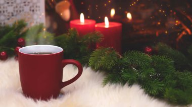 Yeni yılın arka planında kırmızı bardak, şömine, mumlar, Noel ağacı çelengi. Şöminenin yanında sıcak bir kış akşamı. Yeni yıl ve Noel şenlik geçmişi.
