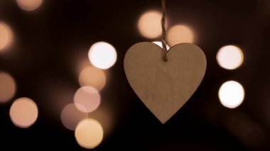 Bulanık bir bokeh arka planda kalp şeklinde ahşap bir Noel oyuncağı. Yakın plan, bulanık arkaplan. Şenlikli yeni yıl geçmişi. Kartpostal, gece görüşü..