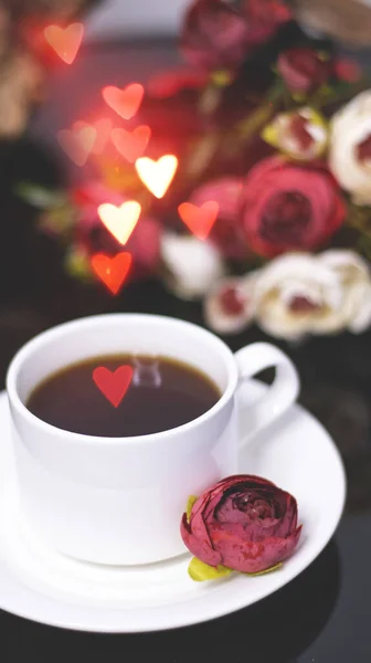 Cup of coffee and flowers. An invitation to a romantic evening. Hearts bokeh, red light effect. Vintage background for postcards.