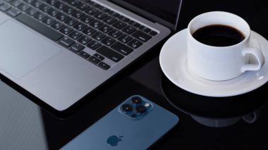 Macbook Apple M1 ve iPhone 12 Pro Max ile karanlık özne minimalist arka planı. Siyah parlak bir masanın üzerinde sade kahve olan beyaz bir fincan. Belarus Gomel - 09.03.2021 