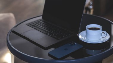 Macbook Apple M1 ve iPhone 12 Pro Max ile karanlık özne minimalist arka planı. Siyah parlak bir masanın üzerinde sade kahve olan beyaz bir fincan. Belarus Gomel - 09.03.2021 