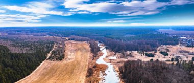 Gökyüzü, tarla ve nehirle kaplı orman manzarası. Bahar güneşli bir gün, vahşi Avrupa doğası. Güzel gökyüzü. Üst görünüm, hava fotoğrafçılığı. 