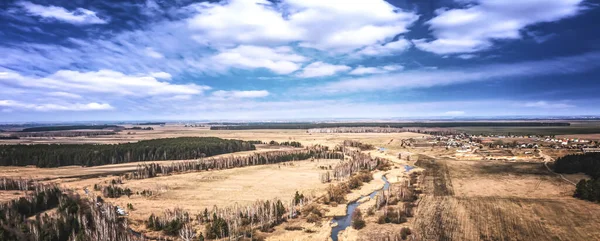 Forest landscape with sky, field and river. Spring sunny day, wild European nature. Beautiful sky. Top view, aerial photography.