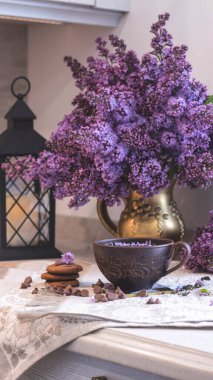 Dekoratif kompozisyon. Mutfağın iç tarafında bir demet leylak var. Bir fincan çay ve çikolatalı kek. Vazoda bir buket leylak. İç kısımlarında leylaklar olan bahar çiçekleri.. 