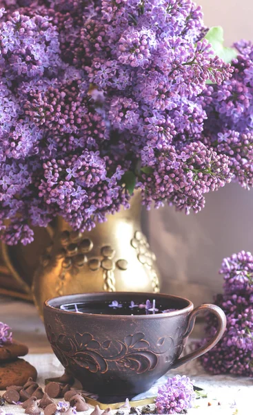 Decorative composition with a Bouquet of lilacs in a light kitchen interior. Clay cup of tea and chocolate cake. A bouquet of lilacs in a vase. Spring floral background with lilacs in the interior.