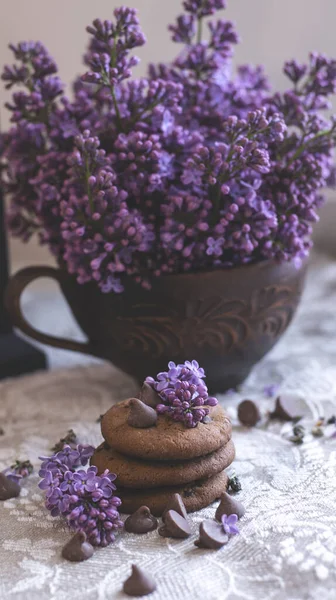 Decorative composition with a Bouquet of lilacs in a light kitchen interior. Clay cup of tea and chocolate cake. A bouquet of lilacs in a vase. Spring floral background with lilacs in the interior.