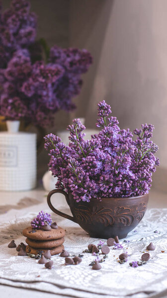 Декоративная композиция с букетом сирени в светлом интерьере кухни. Чашка чая и шоколадный торт. Букет сирени в вазе. Весенний цветочный фон с сиренью в интерьере. 