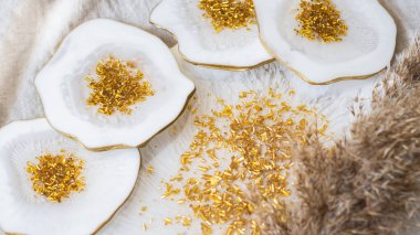 Bardak tutacağı, epoksi reçine tepsisi, taş kesimi, altın kaplama beyaz mermer. Beyaz boya izleri. Masa dekorasyonu, nesne estetiği. Parlatıcı, yansıtıcı. Taş etkisi. Bulanık arkaplan. 